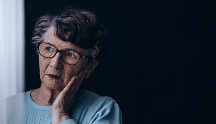 Sad, old woman standing alone in dark room