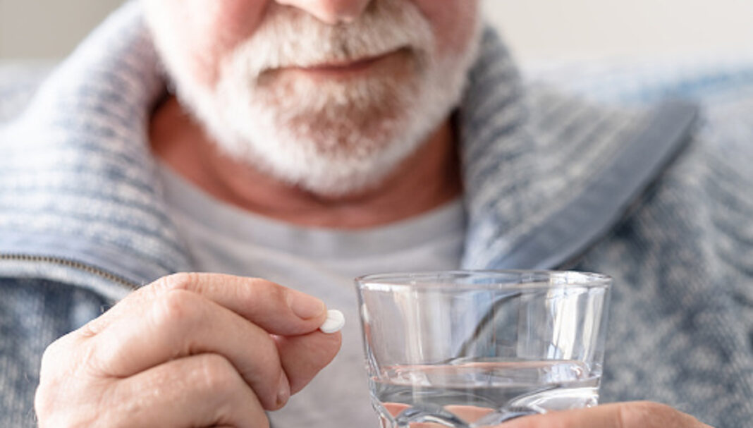Senior man taking a pill with a glass of water - health care and people concept