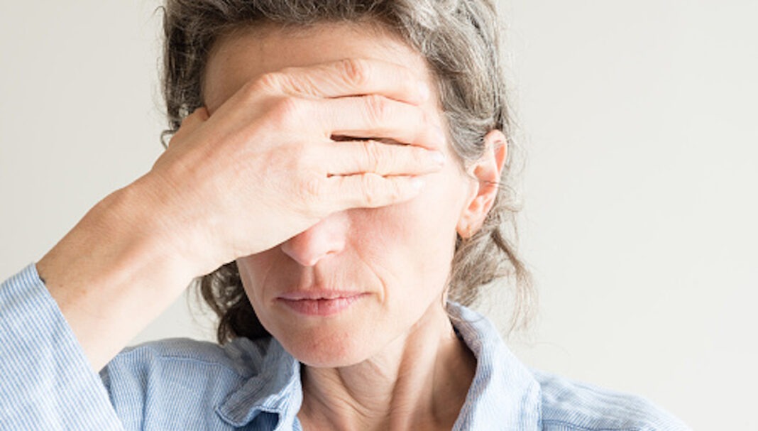 Close up of middle aged woman with hand covering eyes
