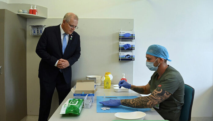 first-vaccine-feature Prime Minister Scott Morrison looks on as pharmacist Branko Radojkovic prepares a simulation of the COVID-19 vaccine at Sydney's Royal Prince Alfred Hospital last week