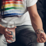 cropped shot of man in t-shirt with pride flag holding glass of water and pill